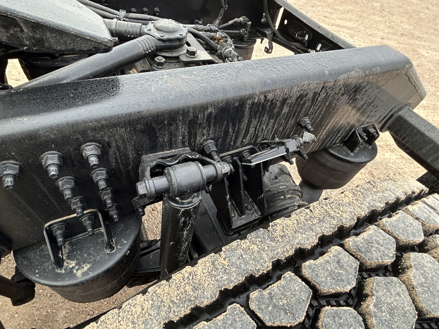 Mack PR64T44 truck chassis showing suspension components and heavy-duty leaf/bolt assembly with dirt on the track and components.