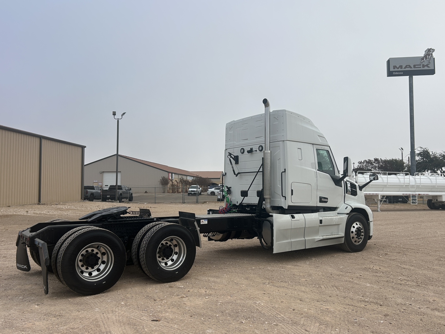 Mack PR64T44 tractor unit in side view showing cab and dual rear axles with empty fifth wheel, white paint, with dealership sign in background.