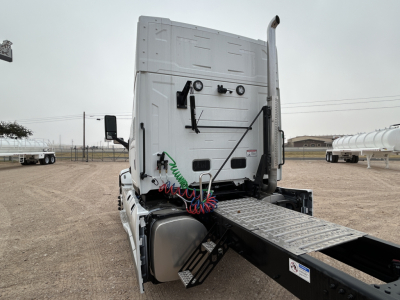 Rear view of a new 2026 Mack PR64T44 truck cab with side-drawn springs, air lines coiled in red/blue, and a metal deck plate for the fifth wheel.