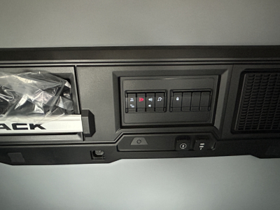 Dashboard area showing switches and controls in a Mack PR64T44 cab interior with storage pocket and vents.