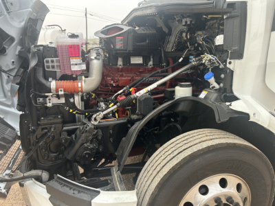 Truck engine bay of a 2026 Mack PR64T44 showcasing the red engine block, hoses, and surrounding components visible from the left front side.