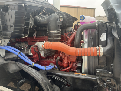 Mack PR64T44 truck engine bay showing orange intercooler hose, red engine, blue hose, air intake, radiator, and surrounding components.