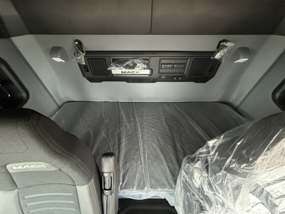 Mack PR64T44 sleeper cab interior showing dashboard area with center console and plastic-covered seats.