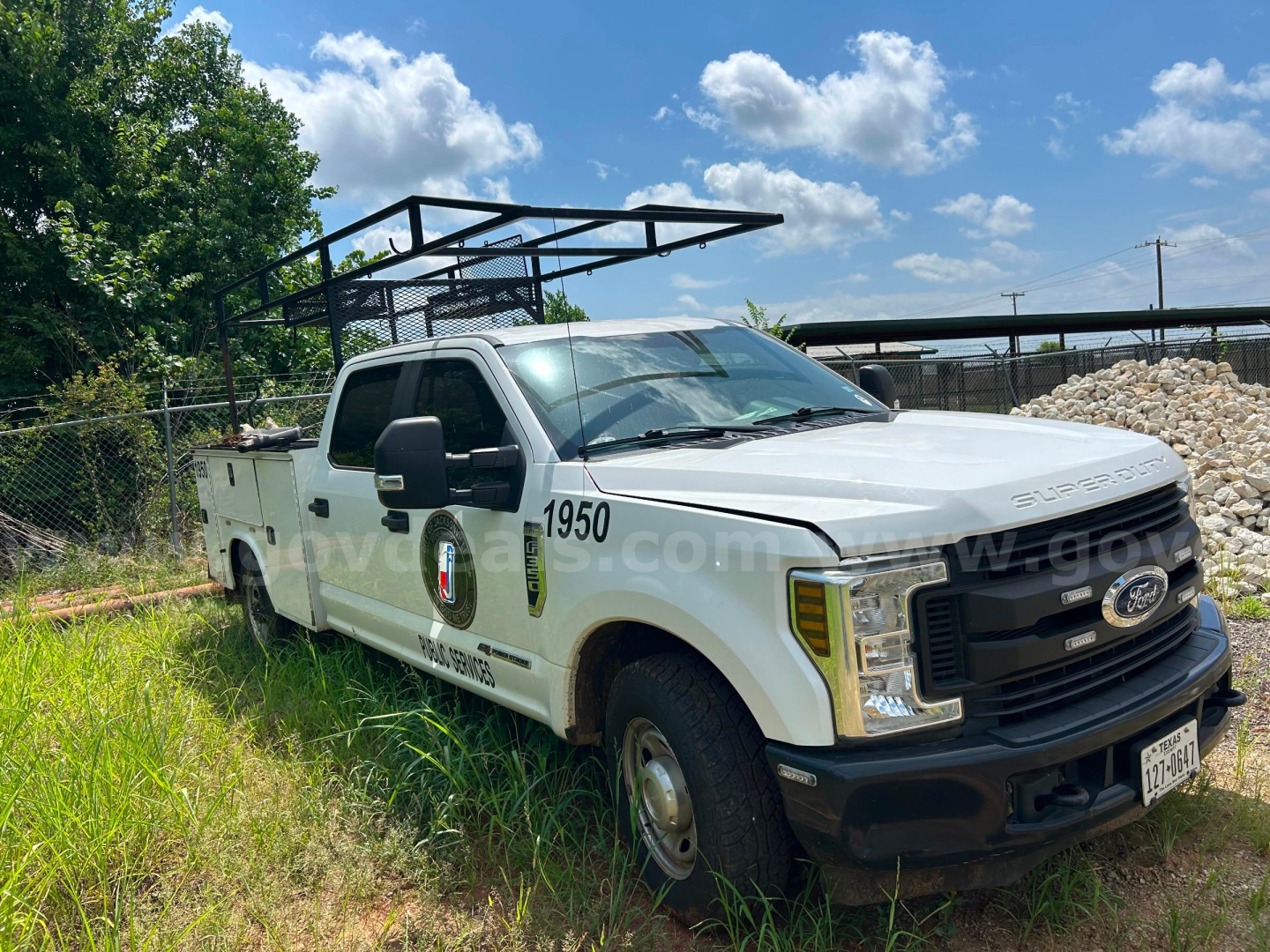 Ford F-350 utility truck in a grassy lot with rack on top; side shows ’1950’ and service markings.