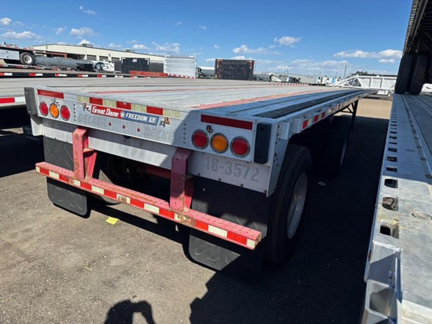 Flatbed trailer rear view showing Great Dane spare and safety rails with red reflectors and bumper, license-area stickers and dual rear tires.
