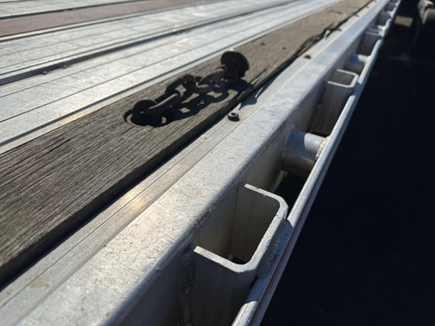Flatbed trailer edge with wooden deck and metal stake pocket visible; part of a Great Dane spread air combo trailer.
