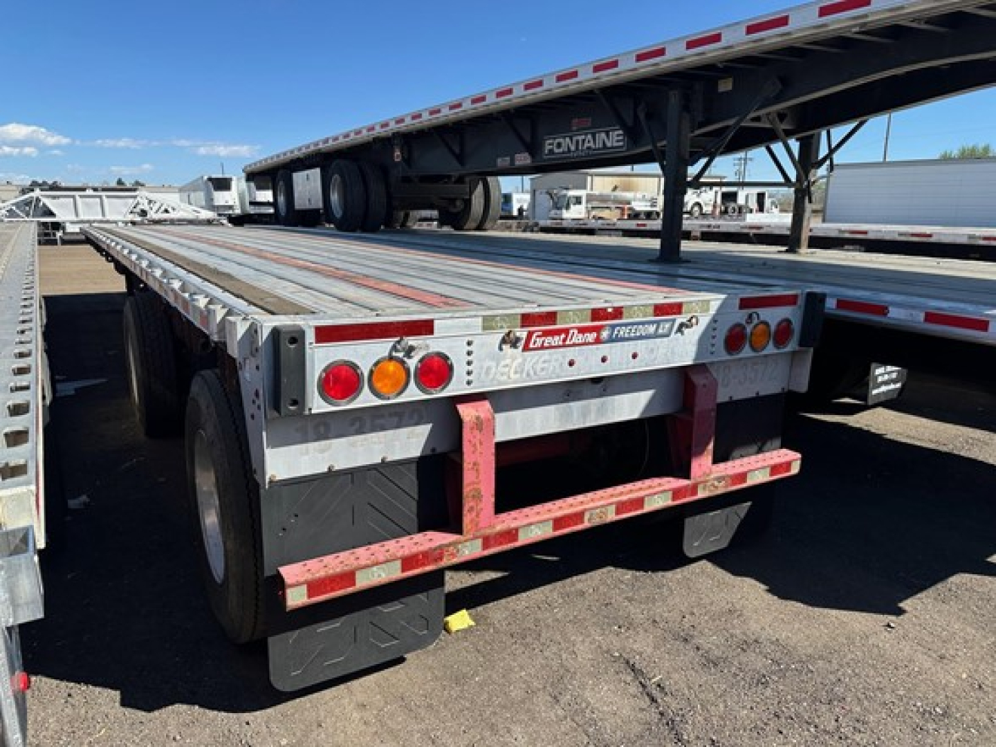 Flatbed trailer rear view showing Great Dane spread air combo with red anti-slip rails and taillights, stock bumper, and dual rear tires.