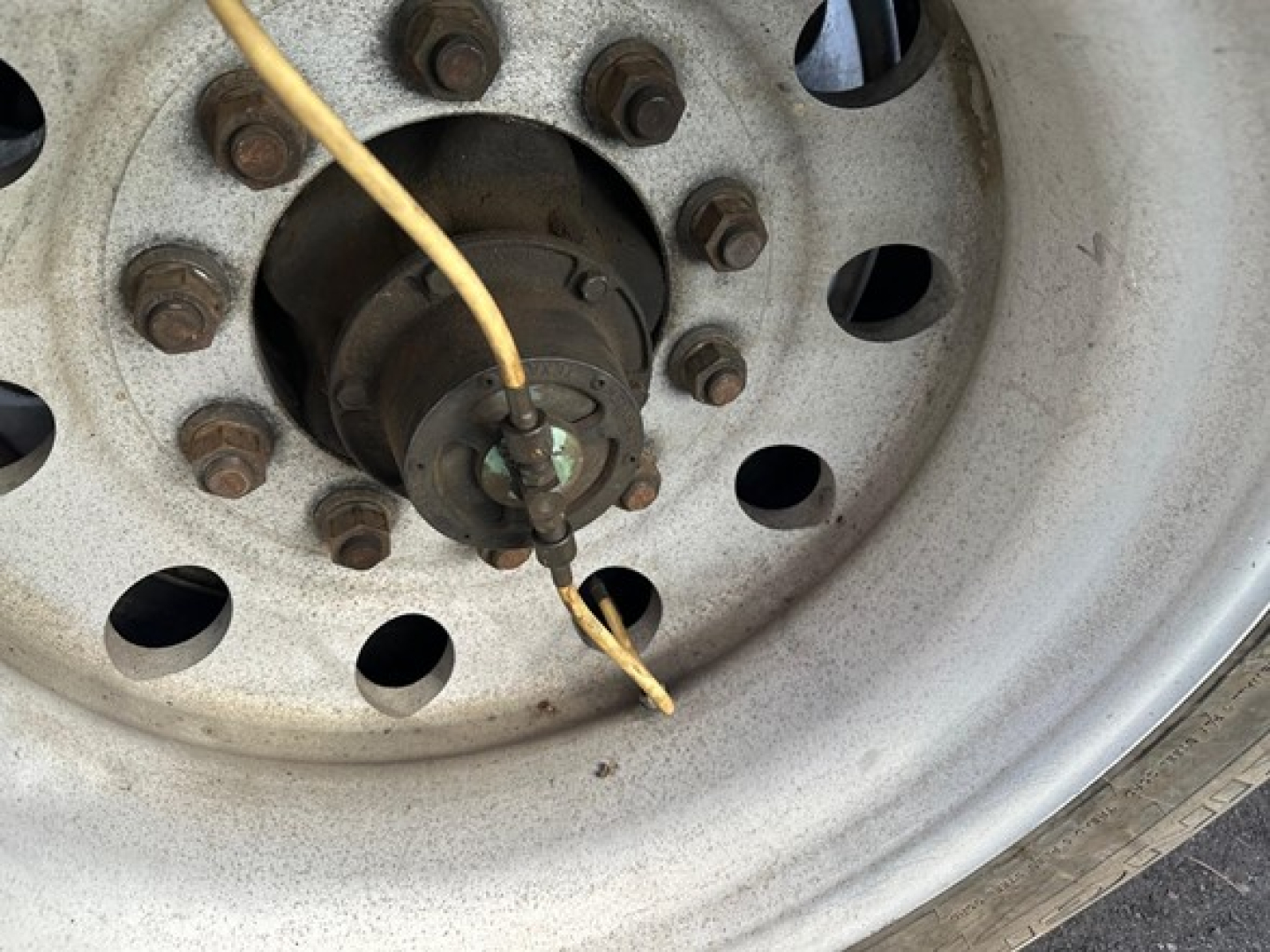 Wheel hub and lug nuts of a Great Dane trailer wheel showing a knotty electrical line tied to the hub and exposed wiring.