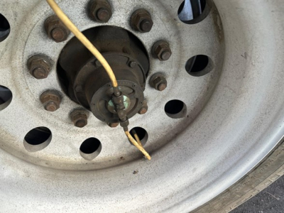 Wheel hub close-up on trailer showing lug nuts and a yellow wire connected to the hub cap.