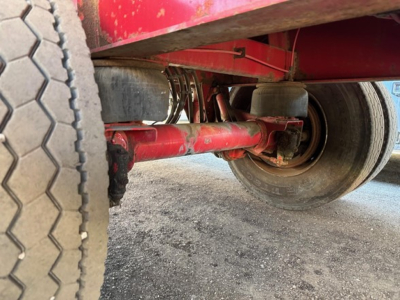 Suspension and axle underside of a red Great Dane trailer showing steel leaf springs, red frame, and wheel with tire tread visible.