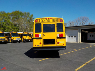 Rear view of a yellow school bus with 'SCHOOL BUS' sign on top and red taillights in a parking lot.