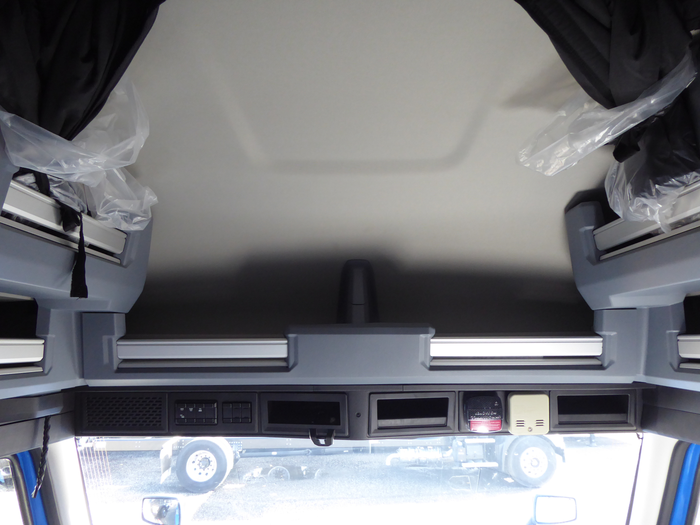 View inside Mack PR64T64 cab showing dashboard controls, storage compartments, and window area.