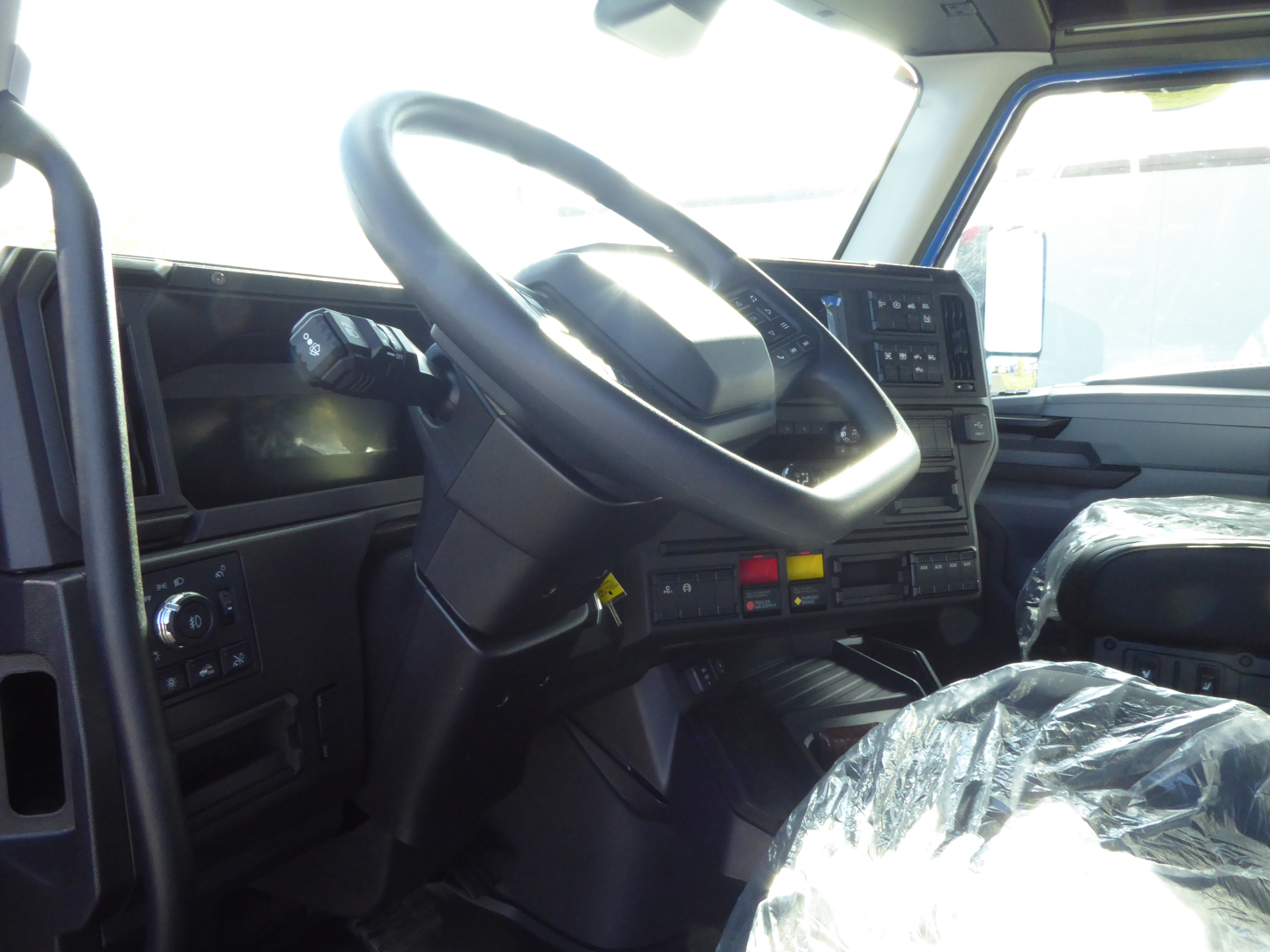 Truck cabin interior: steering wheel, dashboard, and controls visible; plastic-covered seat. No visible labels or text readable besides general dashboard features.
