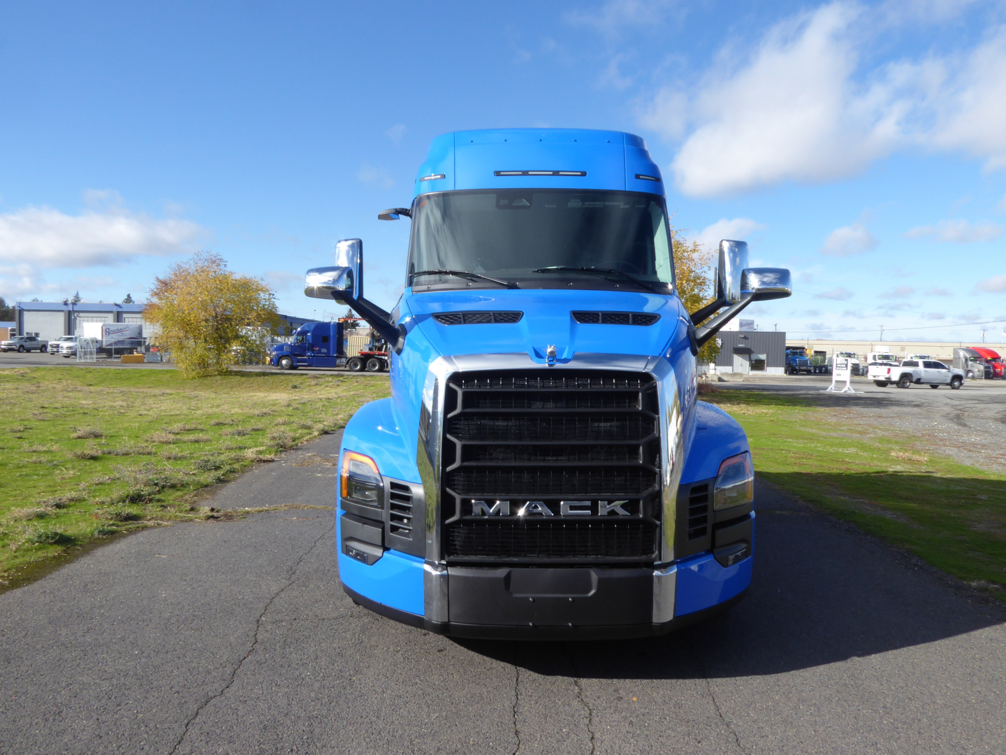 Mack PR64T64 front view truck with blue cab, large grille, headlights, side mirrors; clear sky.