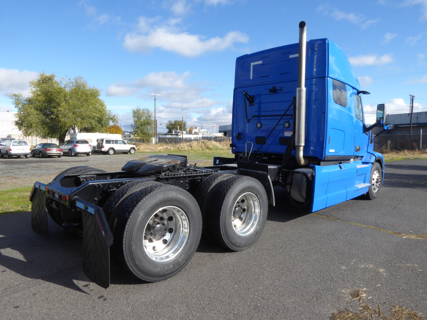 Semi tractor in blue cab, rear view shows dual rear axles and fifth-wheel hitch, clear sky. tractor-trailer prime mover view from left-rear.