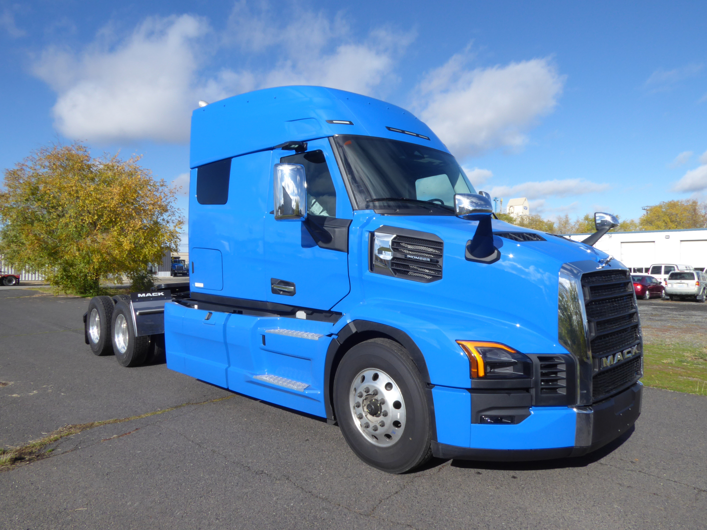 Blue Mack PR64T64 conventional sleeper truck tractor in a parking lot, showing the side and front with chrome grille, black bumper, and tandem rear wheels.