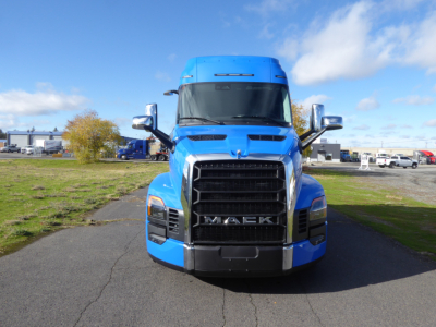 Mack PR64T64 front view truck with blue cab, large grille, headlights, side mirrors; clear sky.