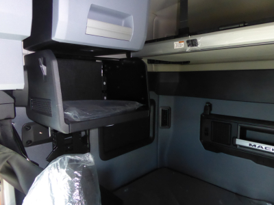 Interior cab area of a Mack PR64T64 truck showing a storage compartment and passenger dashboard with plastic seat wrap.