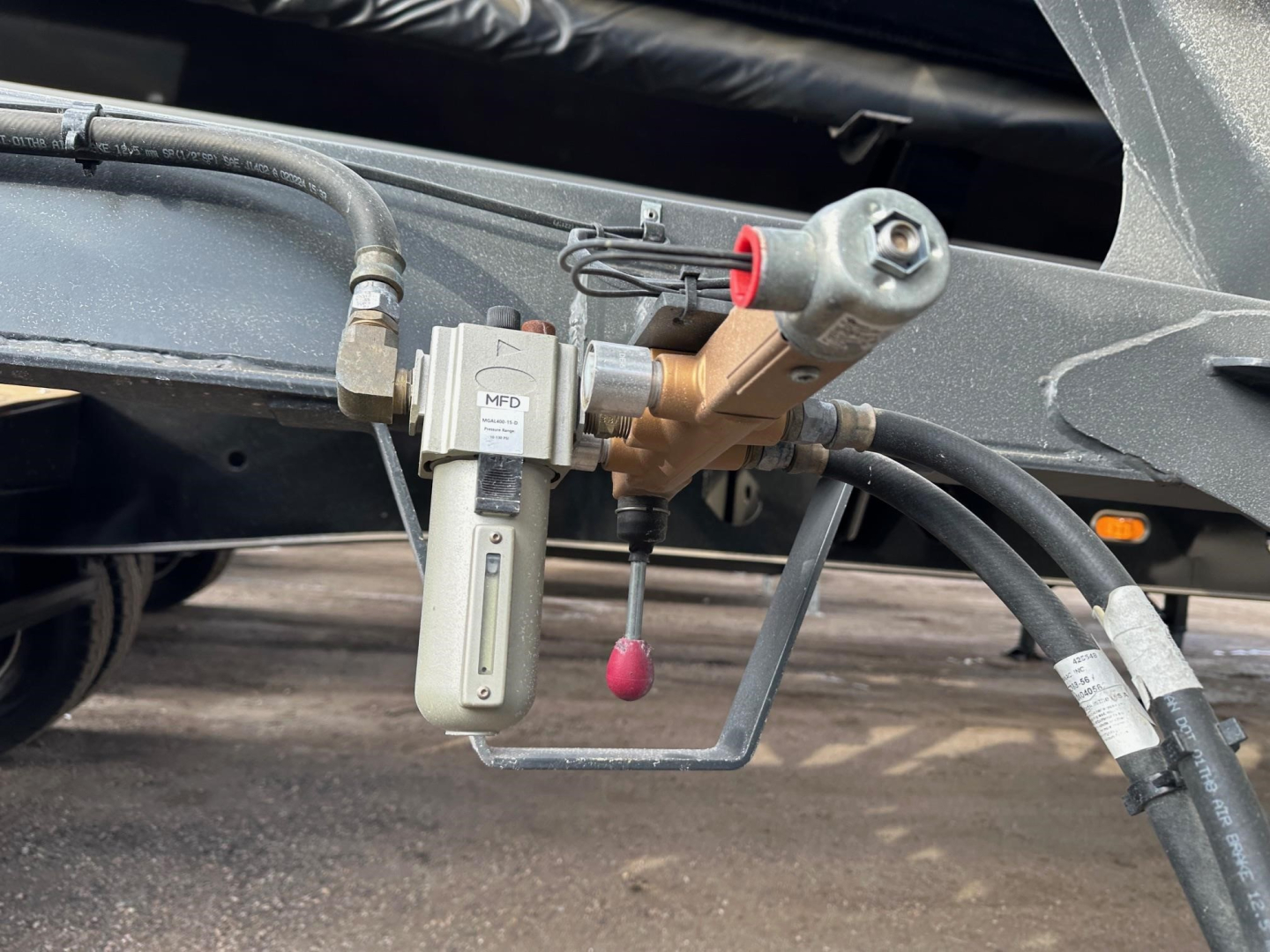 Trailer hydraulic manifold with pump and hoses showing fittings and a small vertical reservoir cap, attached to a frame member.
