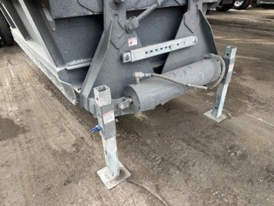 Bottom-dump trailer legs and hydraulic cylinder visible, metal frame with support stands and mounting hardware.