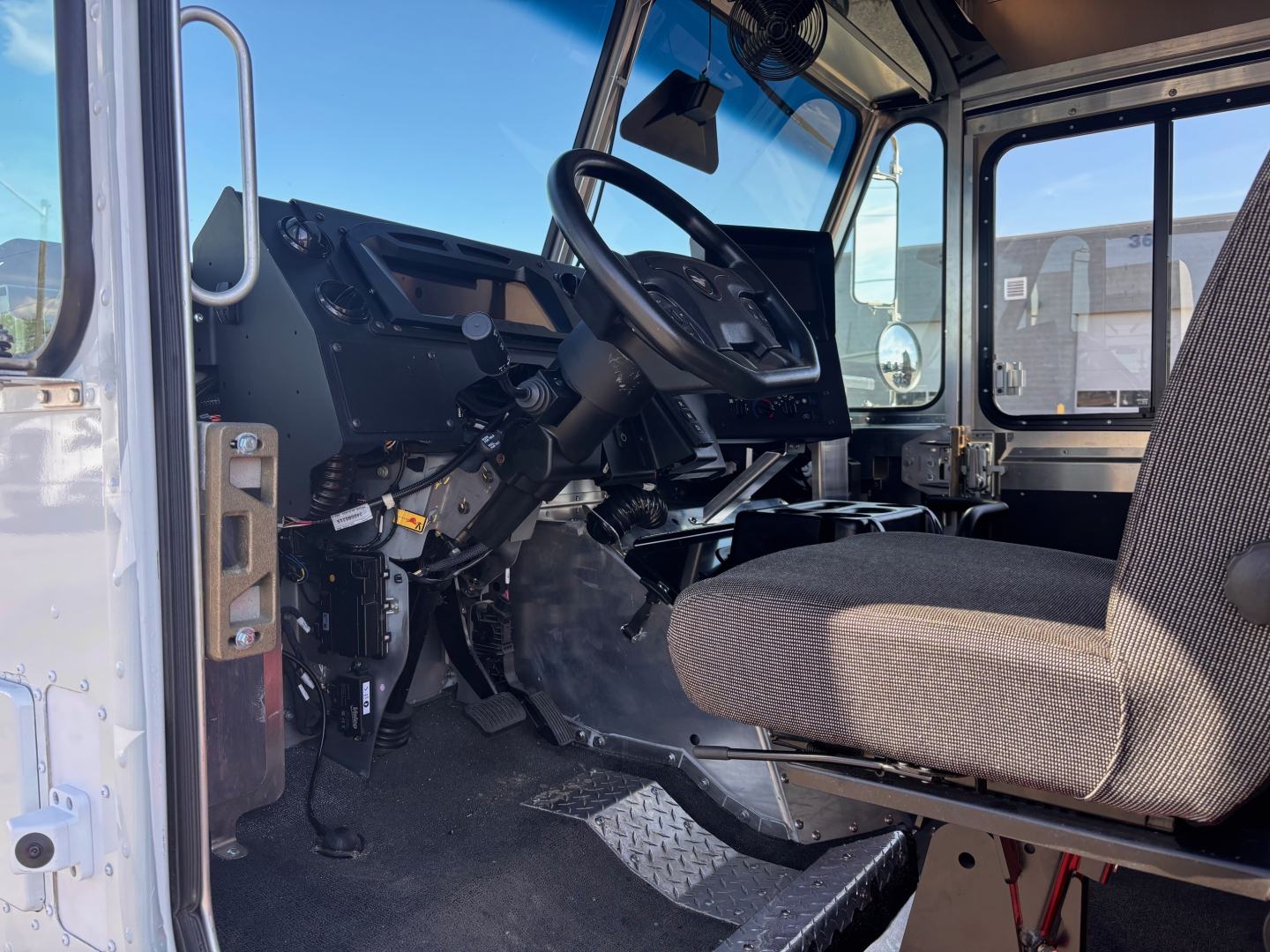 Interior driver area of a 2025 Harbinger S534 step van showing steering wheel, dashboard, pedals, and grey fabric driver seat.
