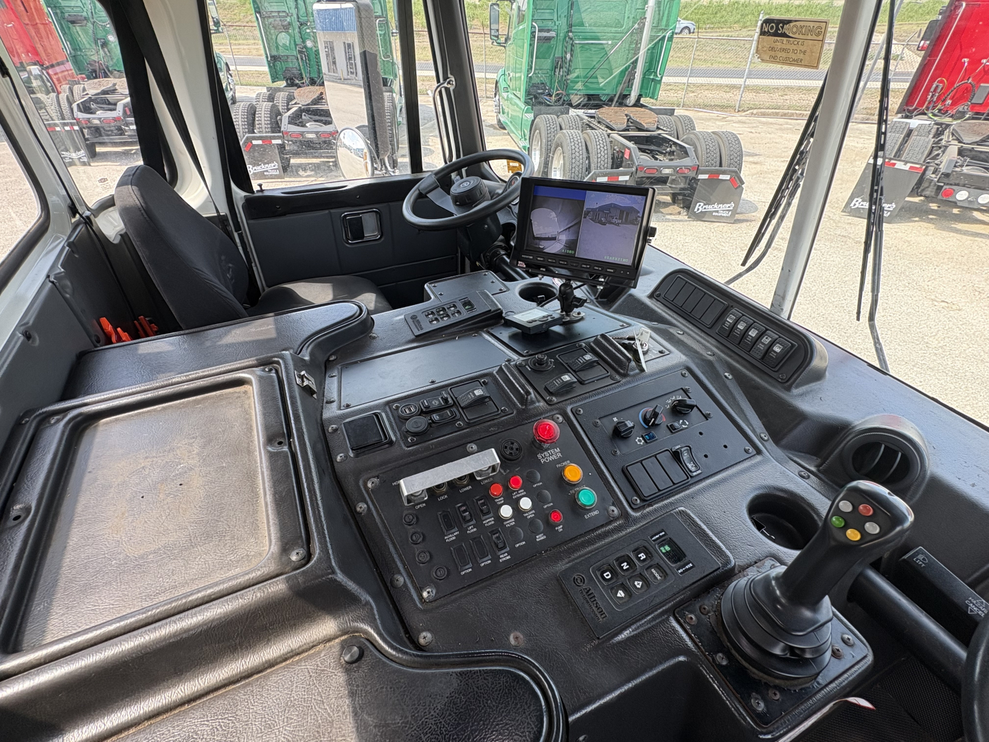 Cockpit of a 2019 Autocar XPEDITOR showing control panel with multiple switches, a joystick, and a monitor displaying camera feeds.