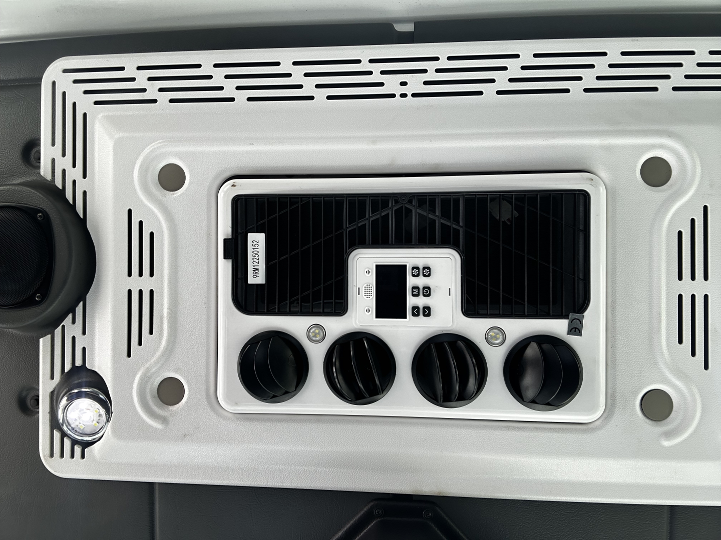 Tractor-style vehicle dashboard console with control panel and four knurled knobs, centered display, and surrounding silver bezel.
