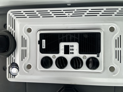 Tractor-style vehicle dashboard console with control panel and four knurled knobs, centered display, and surrounding silver bezel.
