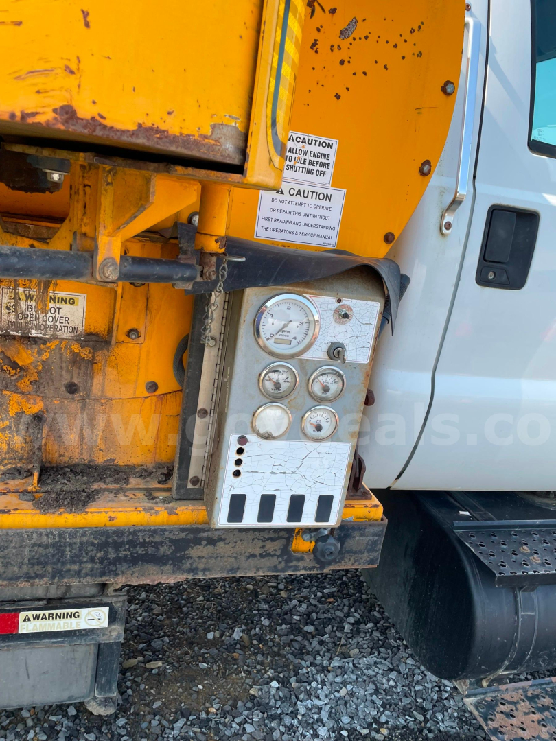 Vehicle side view of a Ford F-750 truck with yellow equipment housing. A metal control panel with gauges and warning labels is mounted on the side near the cab. Visible text includes CAUTION warnings on white labels, and a set of five circu