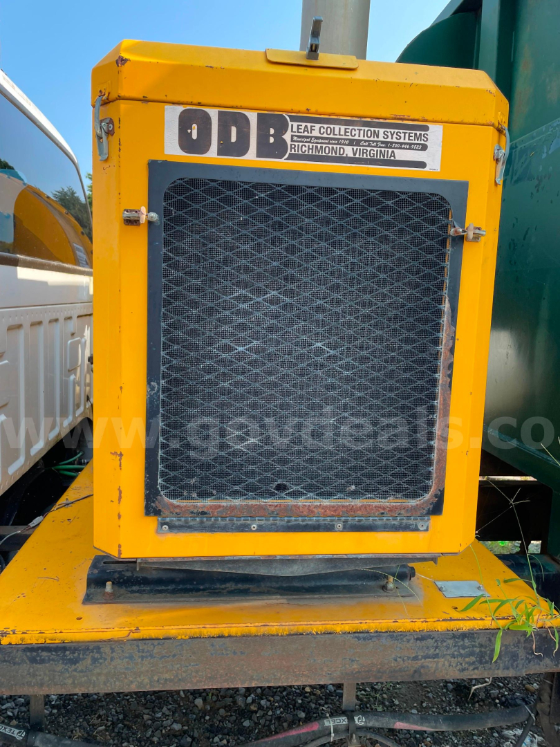 Front view of a yellow Ford vacuum truck with a mesh radiator grille and an ODB Leaf Collection Systems sticker at the top, mounted on a metal platform.