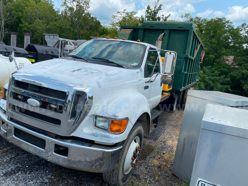 Ford F-750 dump truck in service showing front grille and right side with green dumpster body mounted in bed.