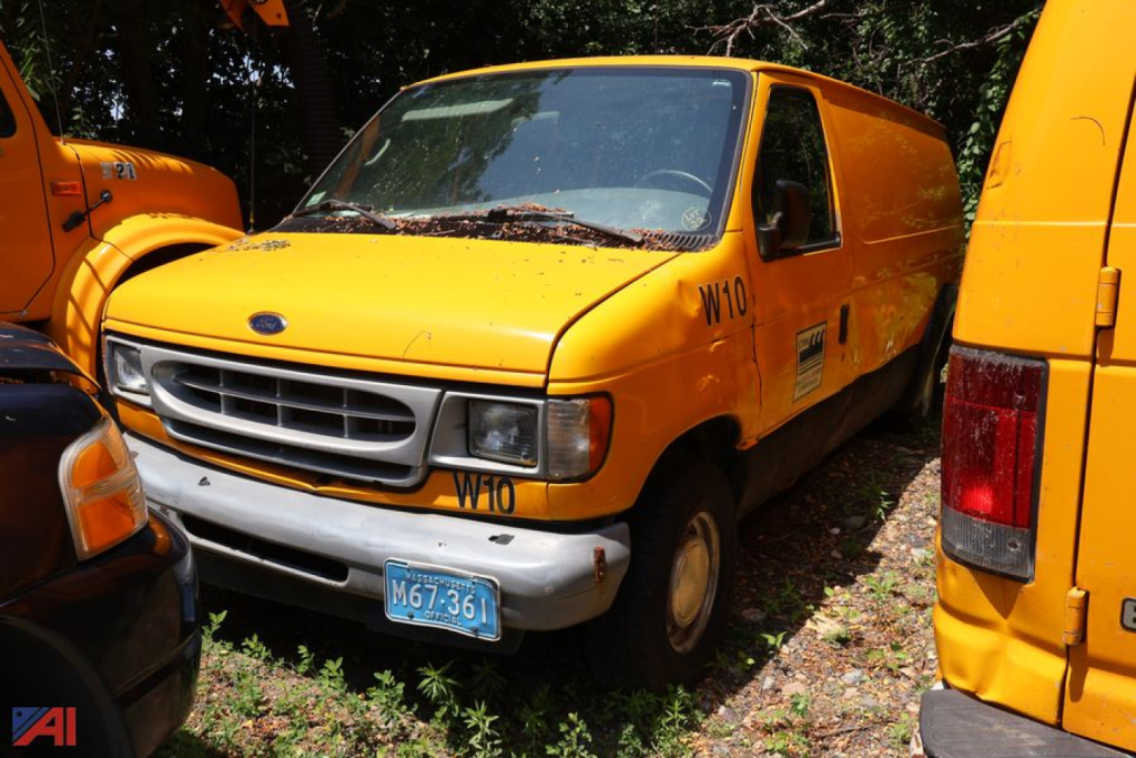 Ford E-Series cargo van in yellow with blue license plate M67-36L, parked among other yellow vehicles; W10 and W10 markings on side; 2002 Ford E150 van.