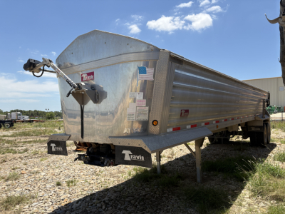 Trailer side and front of a 2024 Travis Wave dump trailer with a front hitch, metal side panels, and a small American flag sticker on the side.