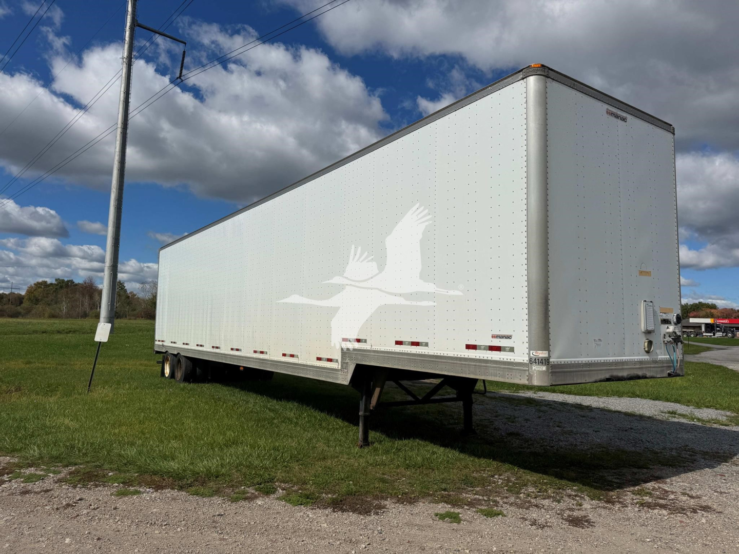 Manac drop deck trailer in side view showing rear entry doors, white dot decals, and landing gear. Side of trailer has a large white marlin or bird graphic and reflective tape along the bottom edge.