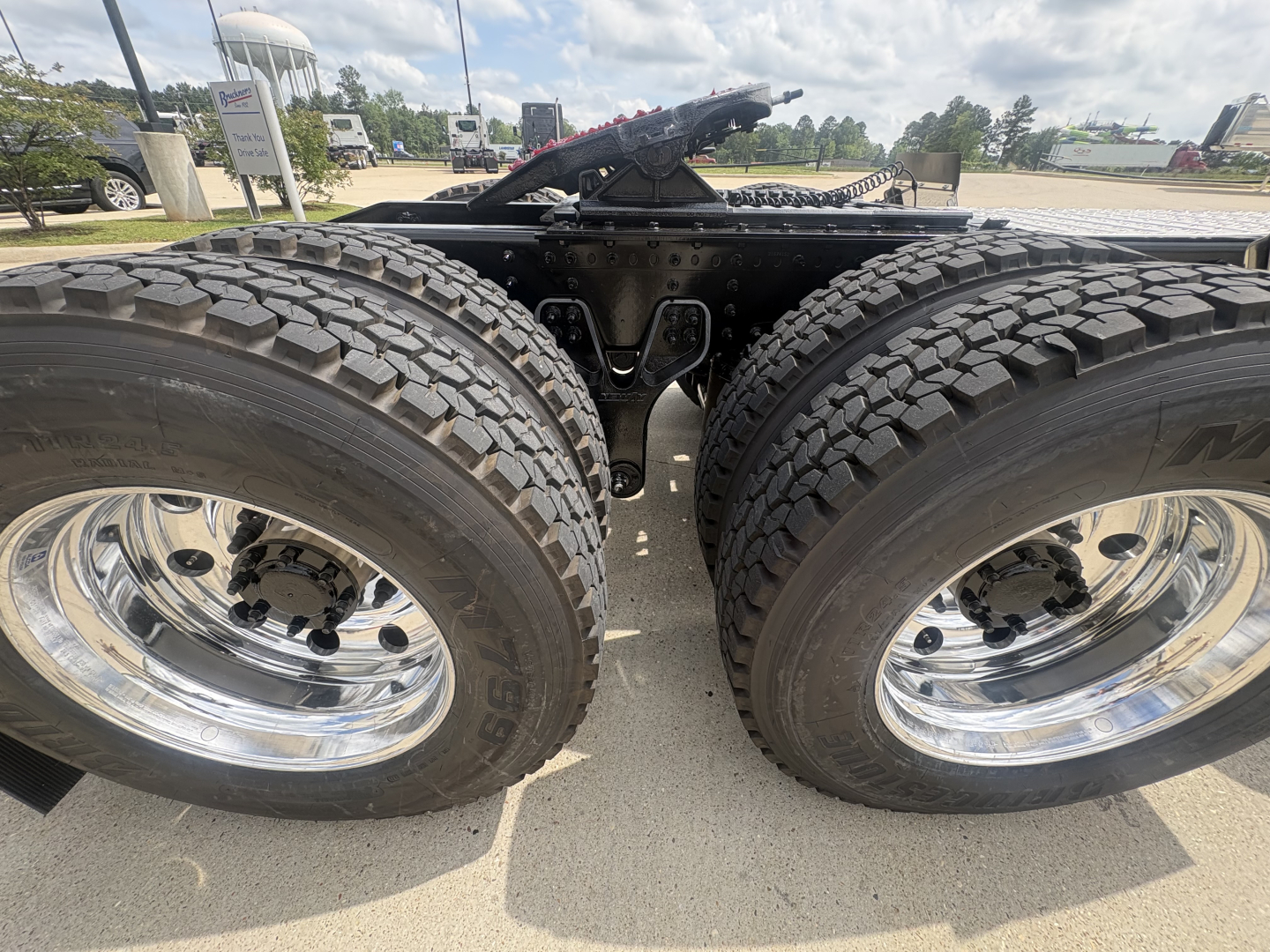 Front view of a new 2027 Mack PI64T conventional daycab chassis showing dual rear axles with large off-road tires and shiny chrome rims.