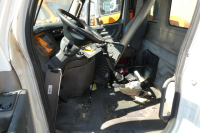 Interior of a Freightliner Cascadia daycab truck cab showing steering wheel, dashboard, and driver's seat with clutter and wear