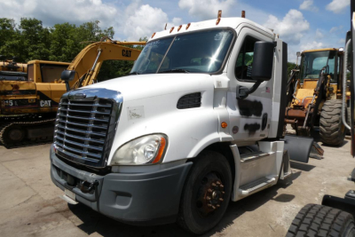Freightliner Cascadia 113 daycab truck in a used lot showing front grille, cab with damage marks, and surrounding heavy equipment.