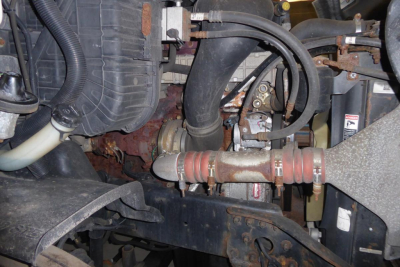 Engine bay with intake hoses and turbocharger pipework visible in Freightliner Cascadia; multiple hoses and clamps; radiator support and front crossmember in view.