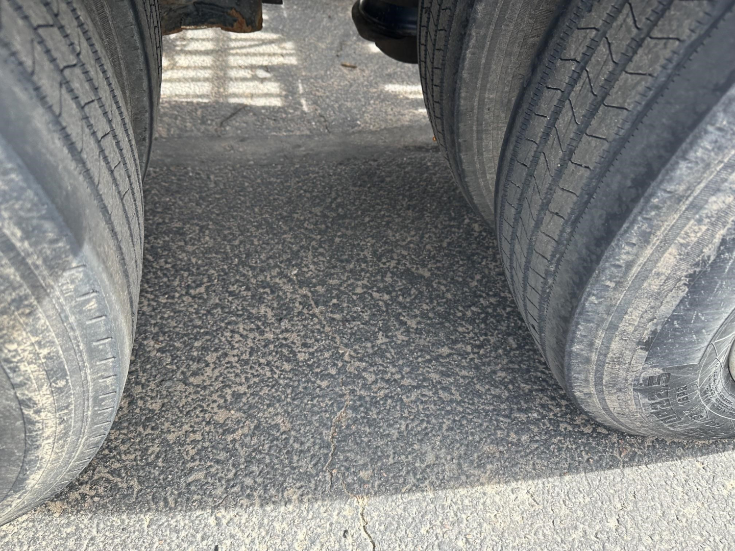 Trailer hitch area showing dual rear tires and roadway surface between axles on a lowboy trailer.