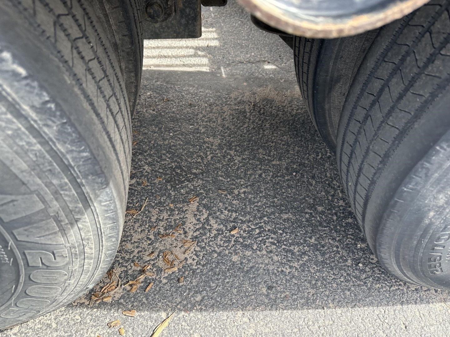 Trailer rear view with dual tires showing tread and road debris between wheels.