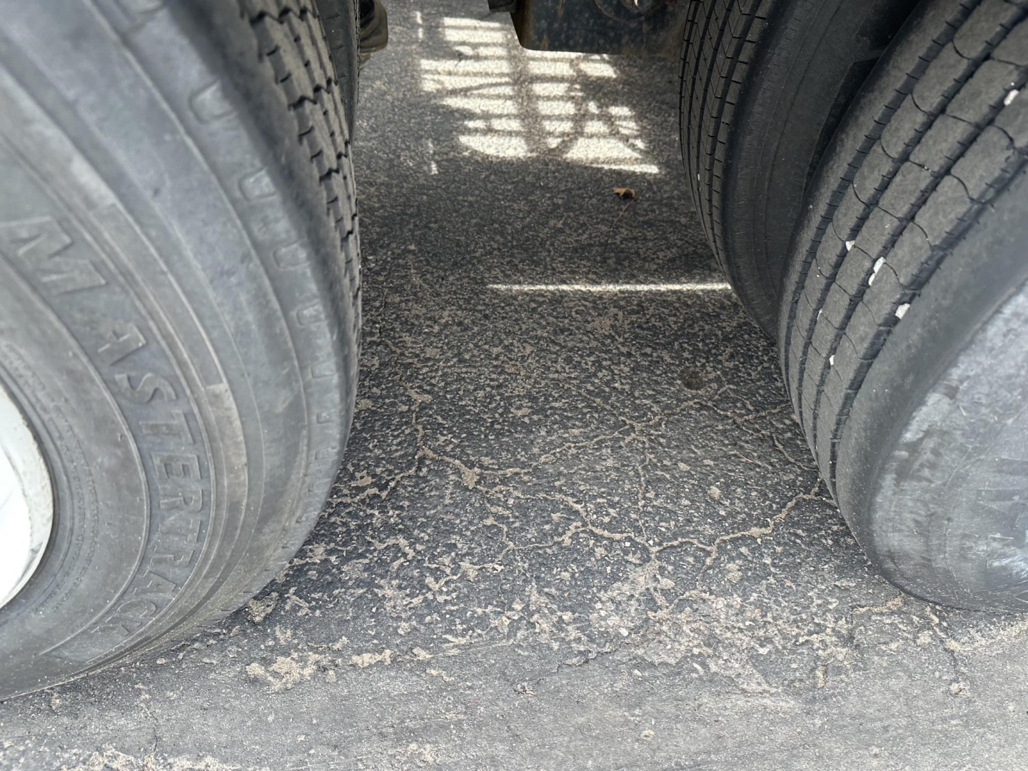 Trailer tires and wheel area of a lowboy trailer showing dual rear tires and dusty paved surface between them.