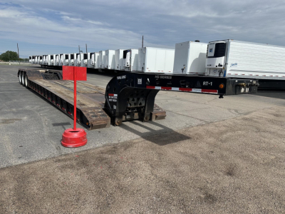 Trail King lowboy trailer with long flatbed and gooseneck. Row of white trailers in background; red pole marker and black gooseneck neck with RT-1 and HG Series markings visible.