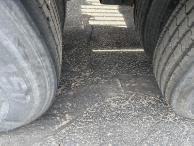 Twin rear tires on a lowboy trailer showing worn rubber tread and dirt on the road surface between axles.