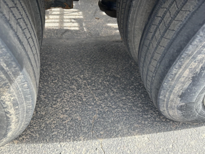 Trailer hitch area showing dual rear tires and roadway surface between axles on a lowboy trailer.
