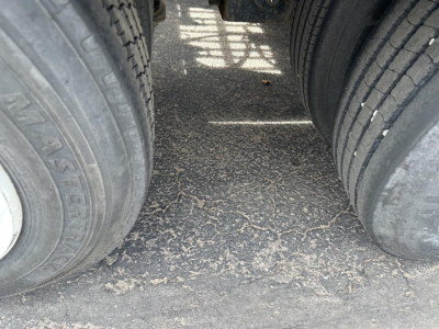 Trailer tires and wheel area of a lowboy trailer showing dual rear tires and dusty paved surface between them.