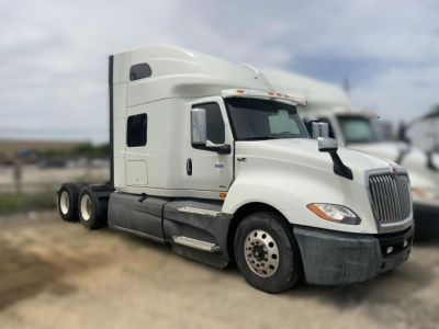 Truck cab showing International LT sleeper tractor with white exterior and chrome grille, side mirrors, and dual rear axles.