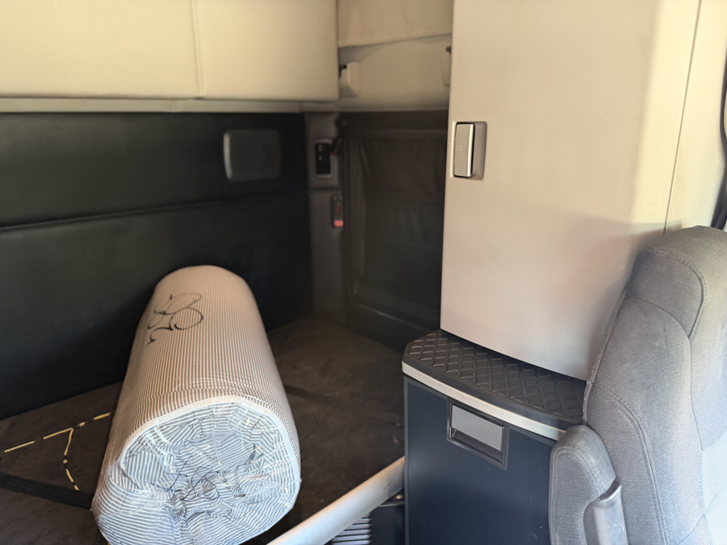 Kenworth T680 cab interior showing sleeper area and storage cabinet with light gray upholstery.