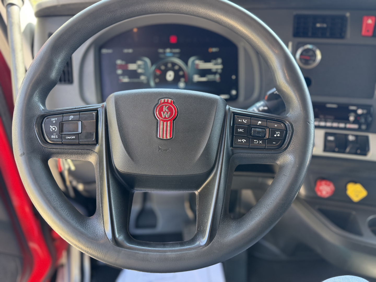 Kenworth T680 cockpit steering wheel with Kenworth emblem, dashboard controls, and instrument cluster visible.