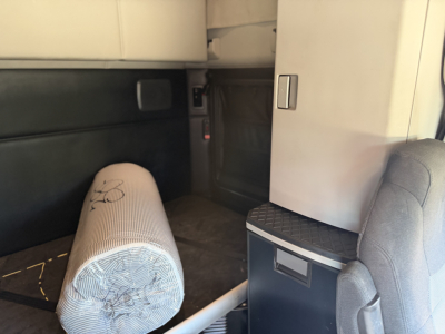 Kenworth T680 cab interior showing sleeper area and storage cabinet with light gray upholstery.
