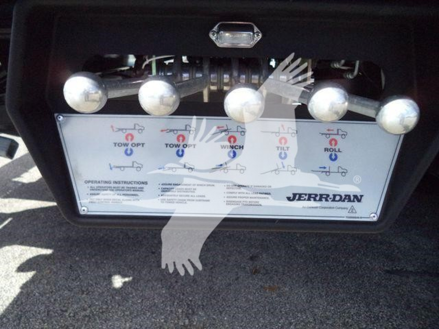 Control panel of a Jerr-Dan rollback equipment with labeled levers and illustration icons for tow/opt operations. Visible text includes 'JERR-DAN' logo and operating instruction panel.